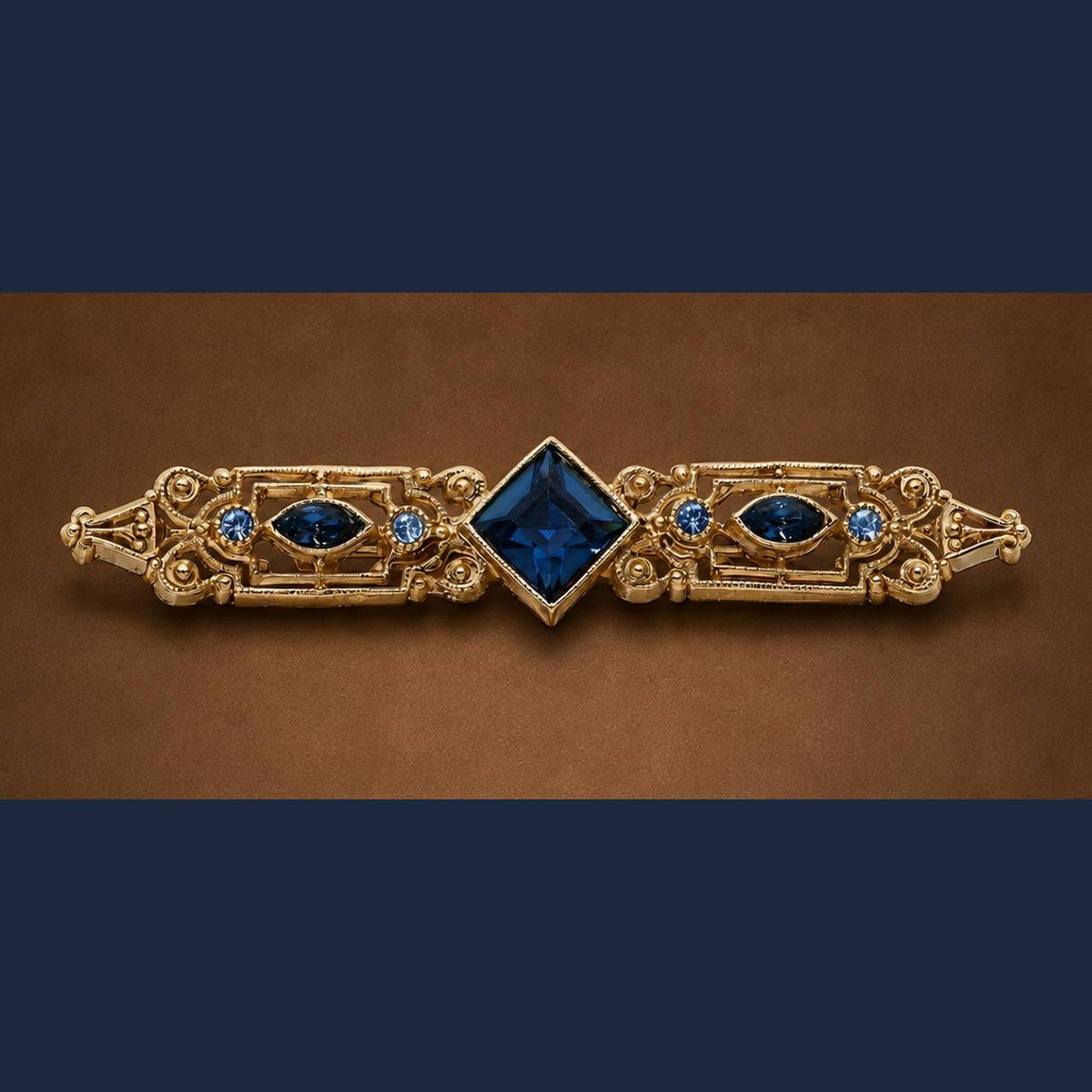 gold fiiigree bar brooch with dark blue diamond shaped center stone and round and oval stones to the side.