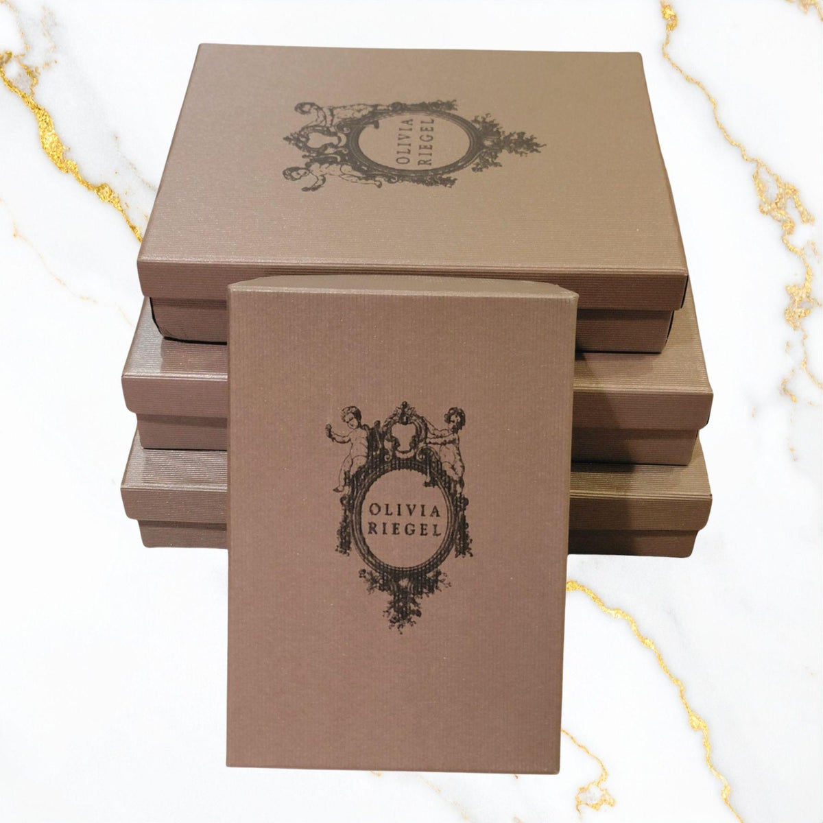 3 stacked OLIVIA RIEGEL gray gift boxes with a fourth leaning against them