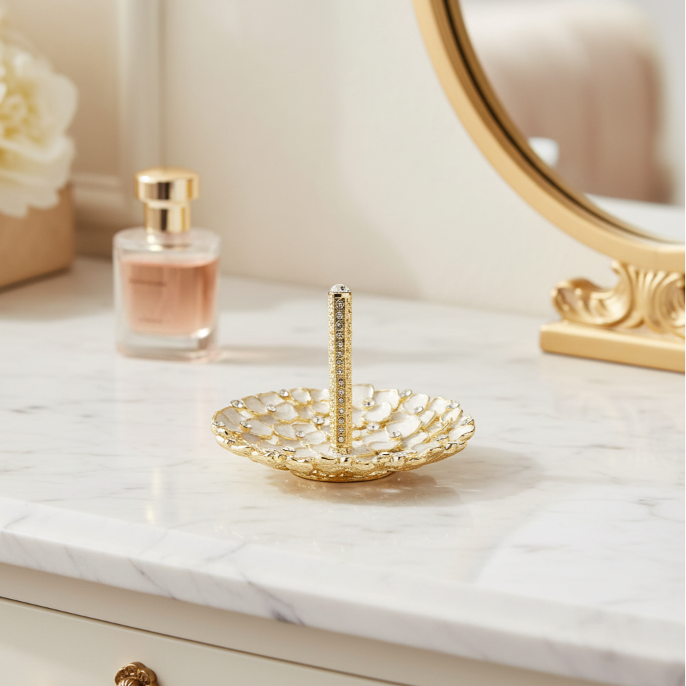 Gold and white Dogwood ring holder on a marble surface with a mirror and flowers in the background